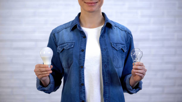 istock Woman choosing between energy saving led bulb and incandescent lamp, efficiency 1159017949