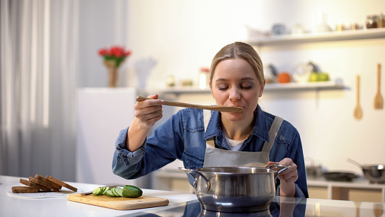 Beautiful lady tasting soup while cooking, preparing food for dinner, dieting