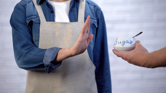 Person in apron gesturing no sugar in cooking, risk of diabetes and obesity