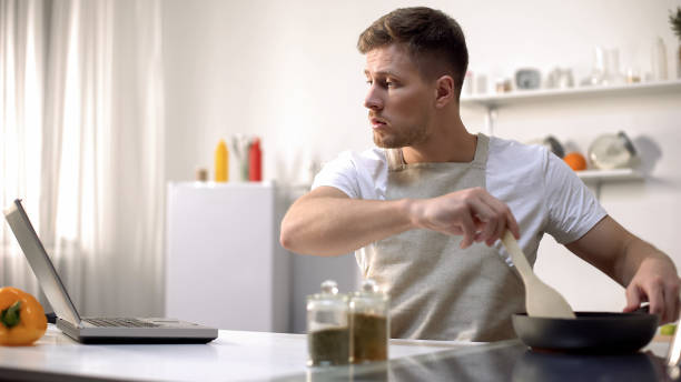 istock Bachelor preparing meal in pan, reading recipe and cooking tips online, courses 1159018174