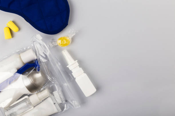 istock Set for flight small bottles with cosmetics, sleep mask, earplugs, nasal spray on gray background. Top view, copy space 1159019279
