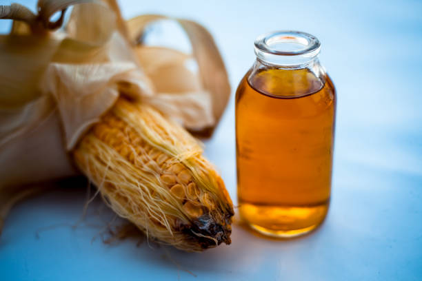 Raw organic corn cob or kernel isolated on white along with its beneficial essential cooking oil in a glass bottle.