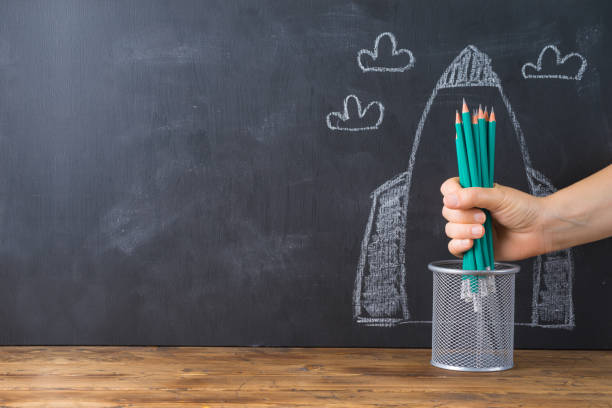 istock Back to school concept with hand holding pencils over chalkboard rocket sketch background 1159034088