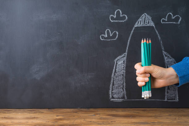 istock Back to school concept with hand holding pencils over chalkboard rocket sketch background 1159034089