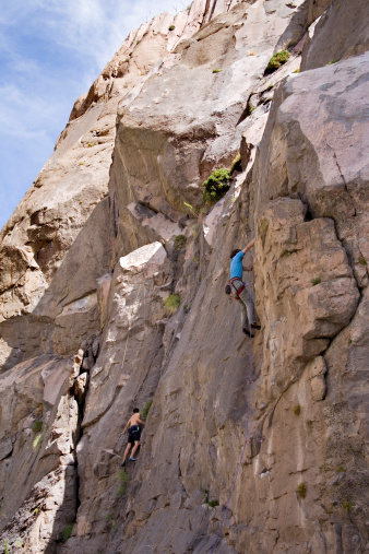 Two male sport rock climbers scaling a shear cliff face in California's Owens River Gorge.