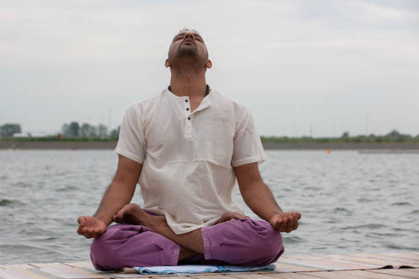 istock Young man doing yoga and meditating in warrior pose on beach 1159037577