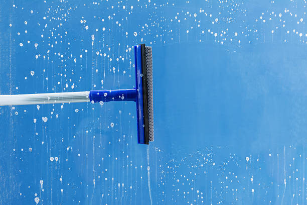 Glass cleaner using a squeegee to wash a window.