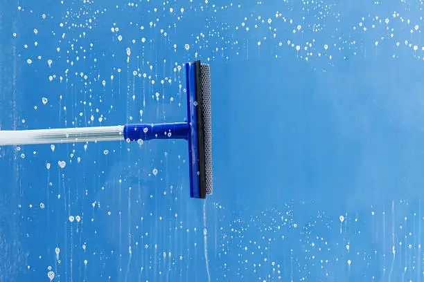 Photo of Rubber squeegee cleans window. Clears a stripe of soaped window. Cleaning service concept.