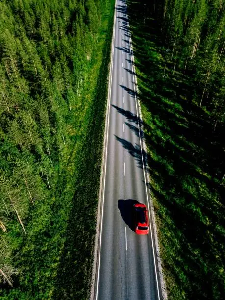 Photo of Aerial view of a country road with red car in the middle of green summer forest