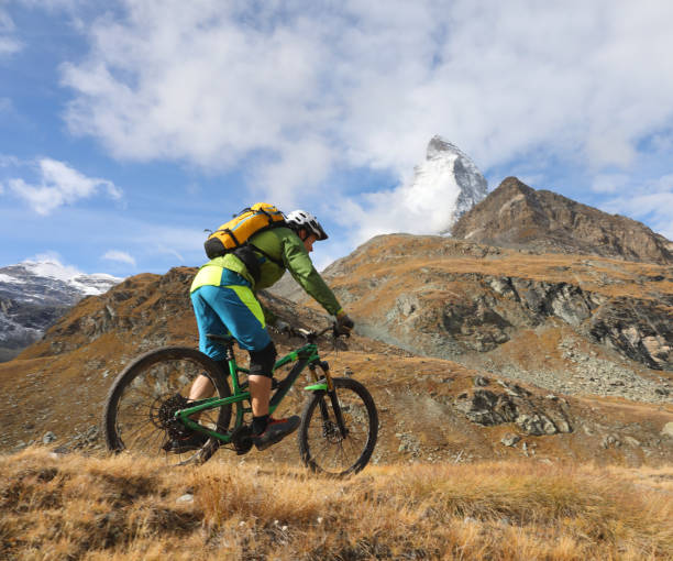 istock Young mountain biker rides through mountain meadow below the Matterhorn mountain 1159058881
