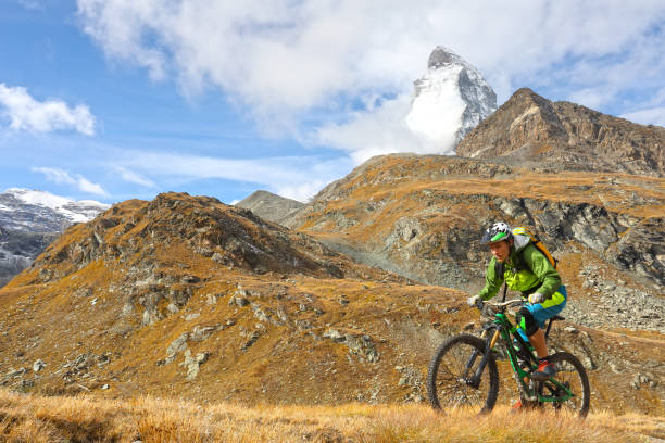 istock Young mountain biker rides through mountain meadow below the Matterhorn mountain 1159058885