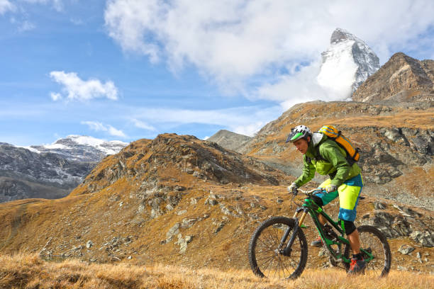 istock Young mountain biker rides through mountain meadow below the Matterhorn mountain 1159058889