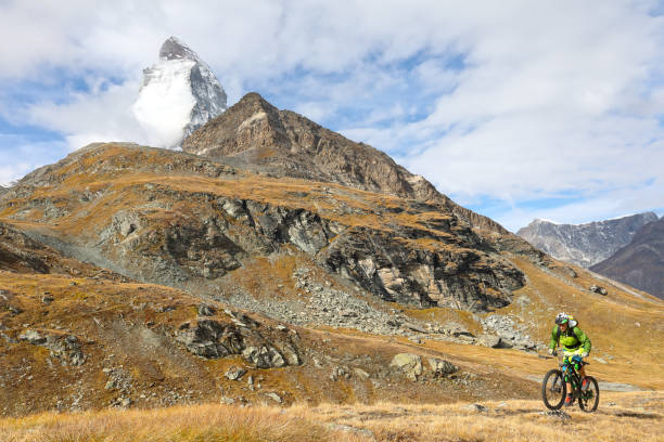 istock Young mountain biker rides through mountain meadow below the Matterhorn mountain 1159058893