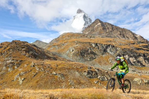 istock Young mountain biker rides through mountain meadow below the Matterhorn mountain 1159058908