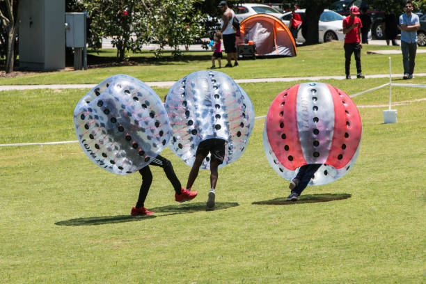 Teenagers Wearing Zorbs Knock Each Other Down At Atlanta Festival Atlanta, GA, USA - July 28, 2018:  Teenage boys wearing plastic zorbs bump into each other and knock each other down at the Atlanta Ice Cream Festival in Piedmont Park on July 28, 2018 in Atlanta, GA. zorb ball stock pictures, royalty-free photos & images