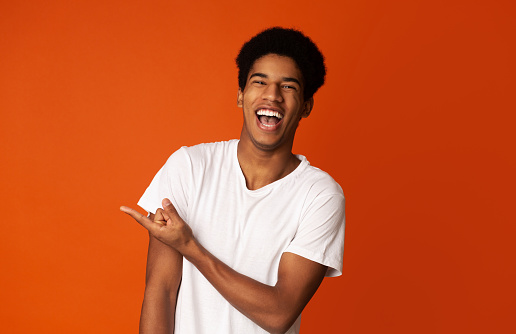 Positive Guy in White T-shirt Pointing Fingers Away at Copy Space over Orange Background