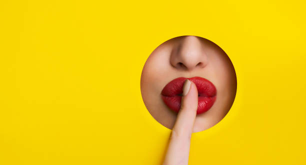 shh! labios rojos miran a través del agujero en papel amarillo - finger on lips whispering secrecy women fotografías e imágenes de stock
