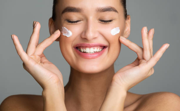 donna felice che applica crema cosmetica sul viso - mettersi la crema foto e immagini stock