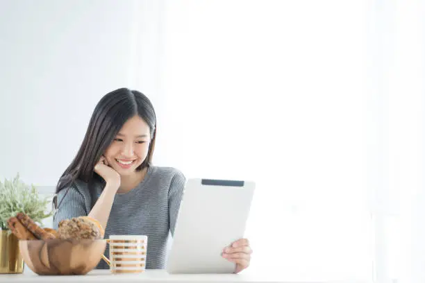 Photo of Young Asian woman using tablet at home and having breakfast in the morning .She reading on tablet.