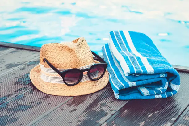 Photo of Vintage summer wicker straw beach hat, sun glasses, blue towel near swimming pool, tropical background