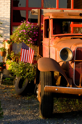 This faded, old, red truck now serves as an interesting prop outside a quaint antiques shop, carrying an assortment of flowers, nicknacks, and the American Flag.