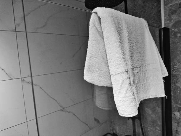 Stock photo showing close-up view of pile of folded, white towels being carried by an unrecognisable person to put on high shelf in a luxury hotel bathroom with horizontal stacked pattern, white bevelled edged wall tiles. Home furnishings and bedroom interior design.