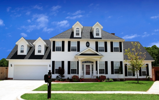 Oak Park, IL, USA - April 5, 2020: A new, white modern farmhouse with a dark shingled roof and black windows. The right side of the house has a light rock siding.