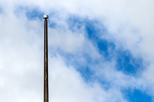 A large, empty flagpole, against a partially cloudy sky. The flagpole is metal, but does not have a flag or rigging.