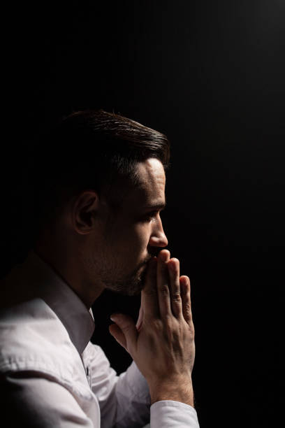istock Handsome bearded man praying. Low light portrait. Black background. 1159082216