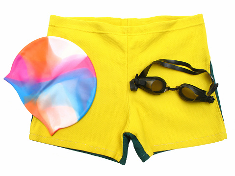 Isolated swimmer's accessories, includes swimming shorts, multicolor cap, goggles.
