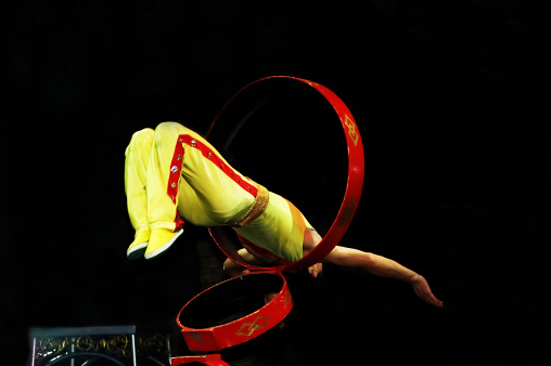 Chinese Gymnist/Acrobat doing a backflip through a small loop 6 ft in the air.