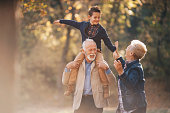 Smiling grandson walking through autumn park with grandparents.