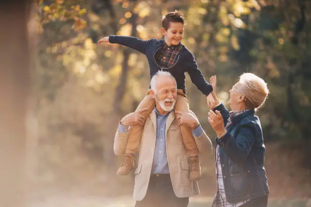 Smiling grandson walking through autumn park with grandparents.