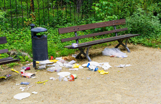 A lot of trash besides a trash can and a brown bank in a park at Dresden, Germany. The litter is most likely due to some birds trying to get some food.