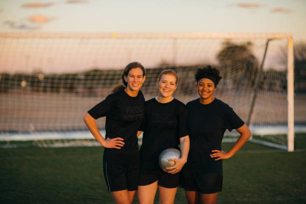 Female High School Soccer Players Three female high school soccer players in practice uniform pause for a candid moment while on the pitch in Arizona, USA. The three friends and teammates enjoy their friendship at dusk with the sun shining through their silhouettes. high school soccer stock pictures, royalty-free photos & images
