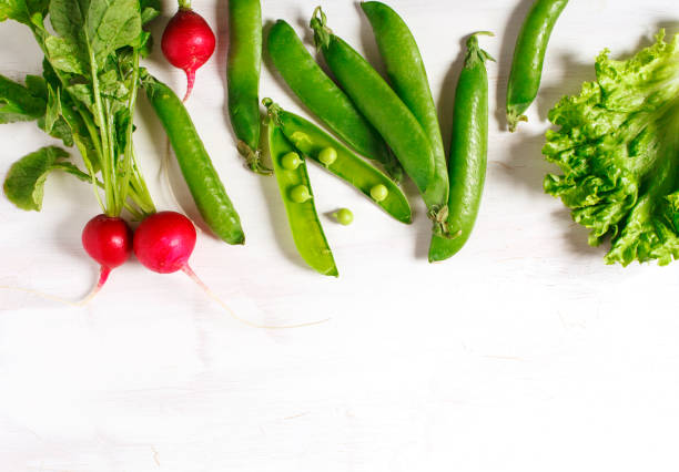 Spring vegetables on white wooden background with copy space. Radish, green peas and green salad - fresh harvest from the garden. Copy space.