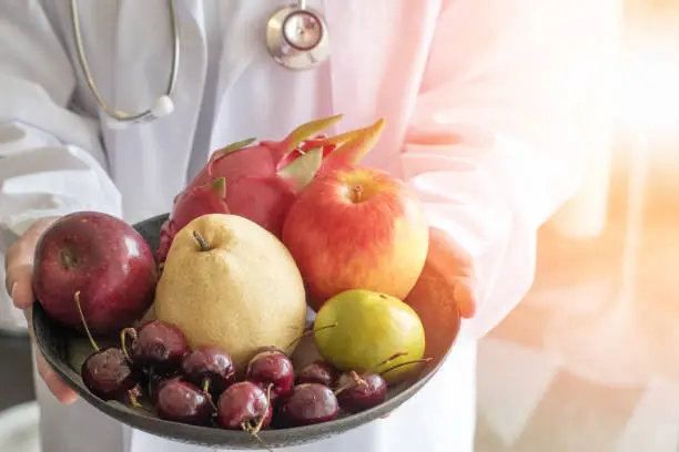 Photo of Doctor or nutritionist hold bowl of fresh fruits of apples, orange, cherry, nashi pear, and dragon fruit with copyspace. Medical healthcare nutrition concept.