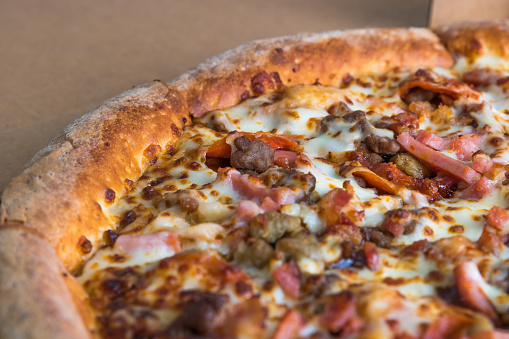 Close up view of a whole sliced delivery pizza pie. Sausage, ham, cheese, pepperoni, tomatoes, and barbeque sauce.