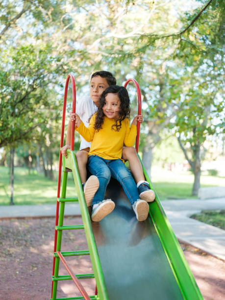istock Boy sliding in a playground with his little sister 1159111690
