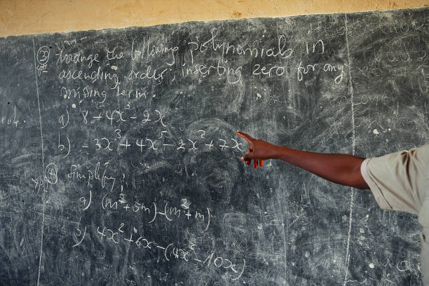 istock Teacher Hand pointing at blackboard with math problems in African school. 1159111747