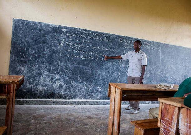 istock Teacher pointing at blackboard teaching in classroom in Rwanda. 1159118210