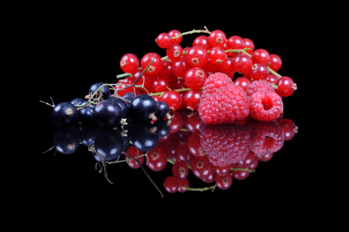 mixed berries and currants on a black reflective background