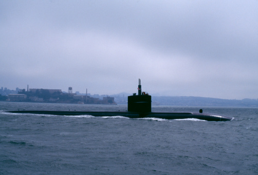 US Navy Los Angeles class submarine slipping out to sea under cover of fog in San Francisco Bay, California, USA. Historical photo from 1996. Alcatraz Island in background. Scanned film, some grain.