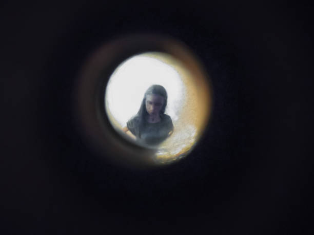 Woman seen out of focus through the old dirty peephole of the front door of an apartment