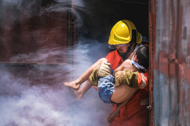 Firefighter holding child boy to save him in fire and smoke,Firemen rescue the boys from fire stock photo
