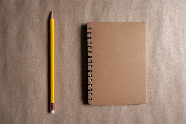 istock Yellow pencil and brown note book on brown paper background 1159142074