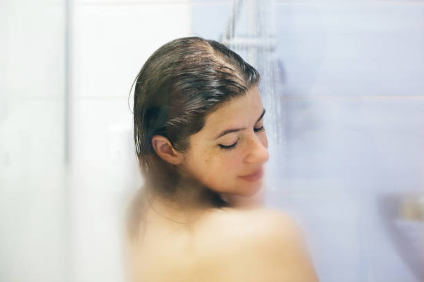 집이나 호텔 욕실에서 샤워를하는 젊은 행복한 여성. 아름다운 갈색 머리 소녀 그녀의 머리를 세척하고 휴식 시간을 즐기고. 신체와 피부 위생, 라이프 스타일 컨셉 - bathtub women naked human face 뉴스 사진 이미지