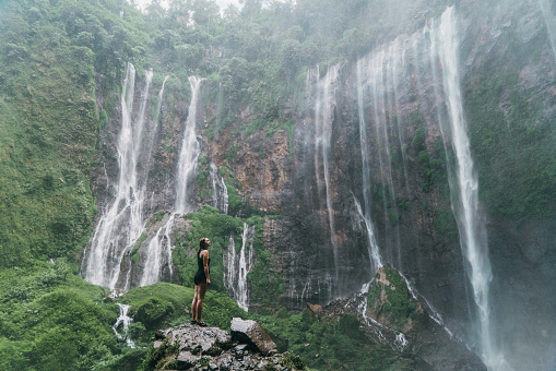 Young Caucasian woman standing and looking at Tumpak Sewu waterfall on Java, Indonesia