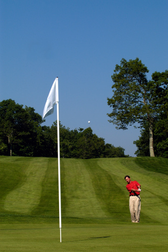 Golfer Chipping onto green towards flag.