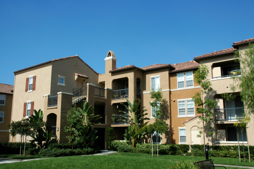 Large three story apartment complex in southern California. Green grass in front and clear blue sky in background.